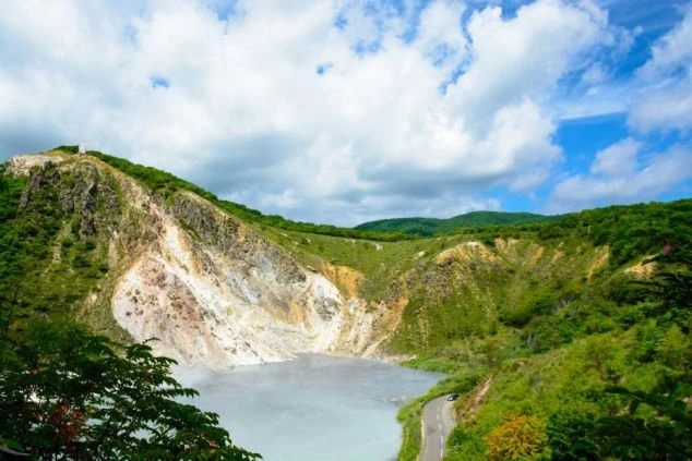 火山のクレーター湖。淡い水色の湖面と緑色の荒々しい山肌が広がる絶景のイメージ画像。リゾートバイトの休日を満喫。
