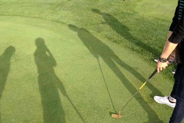 ゴルフ場の芝に映る4人の人物の影の画像。