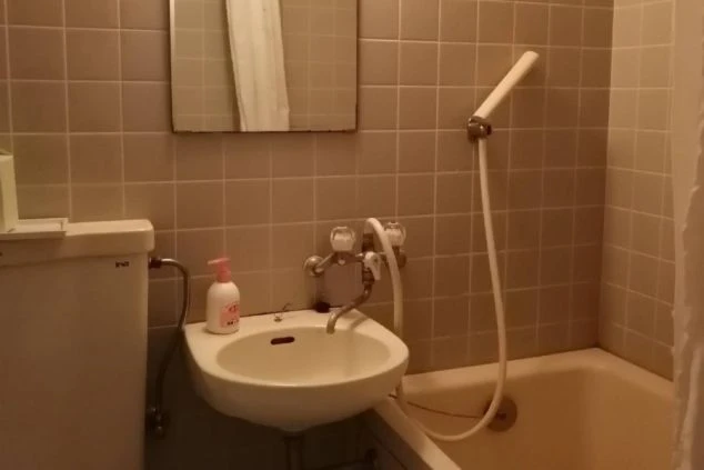 寮のユニットバス。トイレ、洗面台、浴槽、シャワー、鏡が映る清潔な空間。