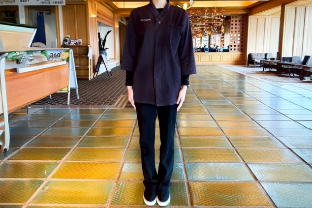 接客係の冬服を着た男性。作務衣のような上着の下に黒い長袖シャツを重ね着している。