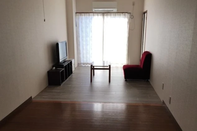 リゾートバイトの1LDK寮のリビングスペース。テレビとローテーブル、赤いソファが置かれ、広々とした空間で快適に過ごせる寮画像。