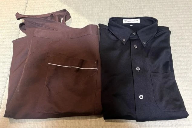 リゾートバイトのレストランスタッフの制服画像。シックな黒のボタンダウンシャツと、落ち着いたブラウンのエプロン。