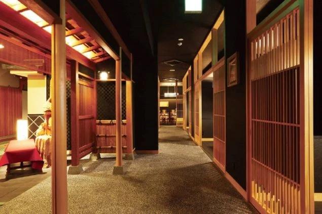 和モダンで高級感のある宿泊施設の廊下。黒い壁と木製の格子戸が、落ち着いた大人の空間を演出している。