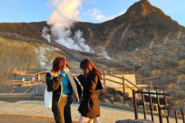 神奈川県箱根・大涌谷の噴煙を上げる山を背景にポーズをとる女性ワクトリスタッフの2人の画像。
