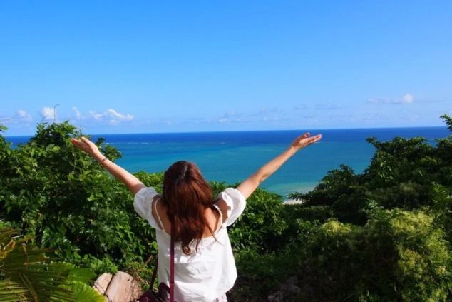 海に向かって両手を広げる女性の後ろ姿の画像。青い空とエメラルドグリーンの海が広がり、リゾートバイトで得られる開放感を表現。