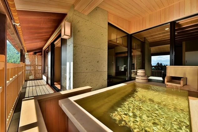 ホテルの客室露天風呂。木製の床と石造りの浴槽があり、窓から山々が見えるイメージ画像。リゾートバイトの休日を満喫。