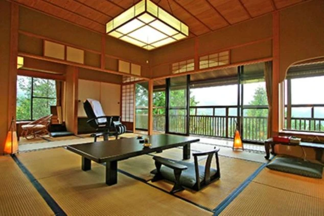 窓から緑豊かな山々が見える和室。低いテーブルと座椅子、マッサージチェアが備え付けられた客室のイメージ画像。リゾートバイトの休日を満喫。