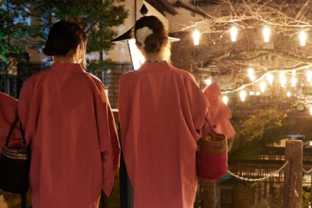 着物姿の女性二人が、ライトアップされた夜の温泉街を歩く後ろ姿。リゾートバイトの仕事の後に、風情ある街並みを散策できることを示す画像。