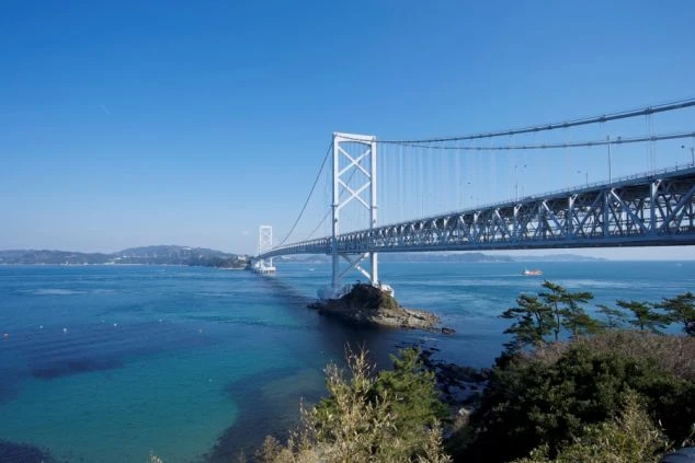 澄み渡る青空の下、エメラルドグリーンの海に架かる真っ白な大鳴門橋の全景。