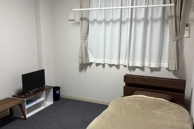 飛騨高山のリゾートバイト個室寮。ベッド、液晶テレビ、テレビボードが備え付けられた清潔な洋室の画像。