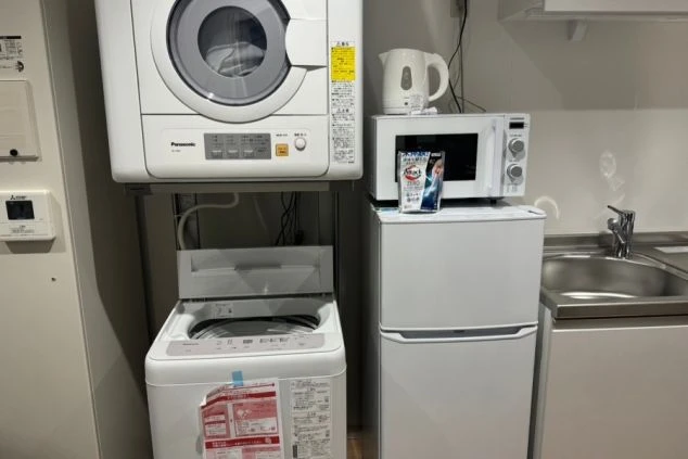 リゾートバイトの個室寮に備え付けられた洗濯機と乾燥機。洗剤も置かれてお生活に必要な家電が揃った便利な設備の画像。
