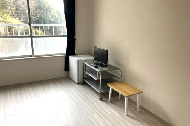 ワクトリの社員が出張で撮影した、リゾートバイトの寮の部屋の画像。フローリングの広々とした空間に、小型冷蔵庫、テレビ、棚が配置されており、窓からは明るい光が差し込む。