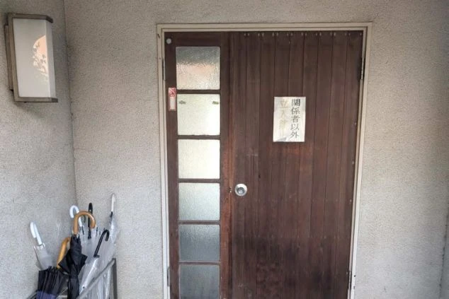 「関係者以外立入禁止」の札がかかった、歴史を感じる寮の木製玄関ドアの画像。