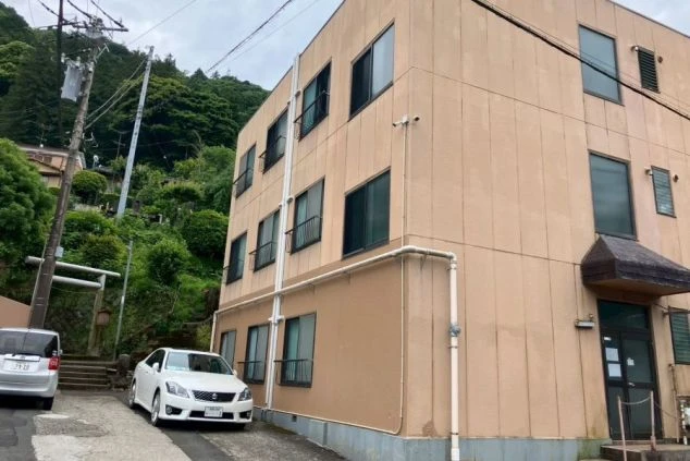 リゾートバイトの女性寮の外観。3階建ての建物で、敷地内に車が停まっている。