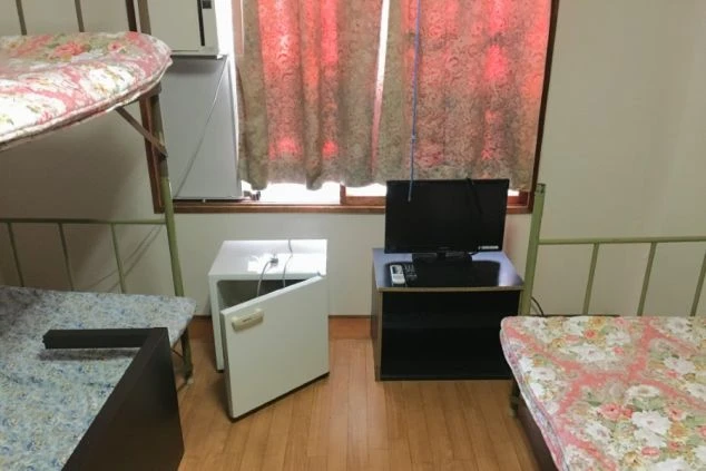 リゾートバイトの相部屋寮の部屋。ベッド、冷蔵庫、テレビが完備されており、リゾートバイトの仲間と共同生活を送る部屋。