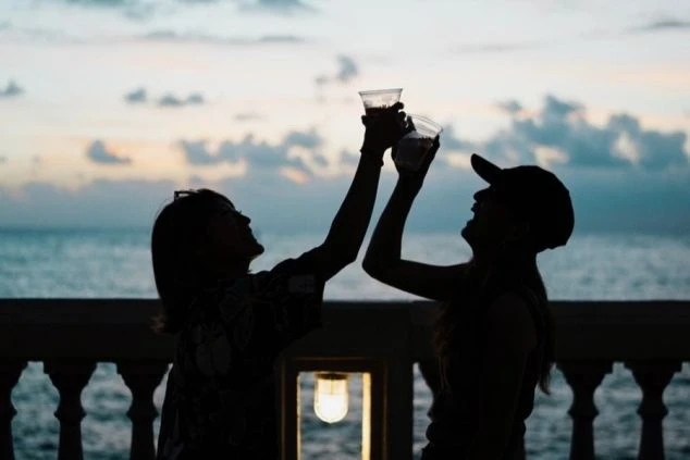 夕暮れのビーチで乾杯する友人同士のシルエット。リゾートバイトで新しい出会いや思い出を作りたい方。沖縄のホテル、飲食店、イベントスタッフなど、人と関わる仕事を探すならワクトリ。