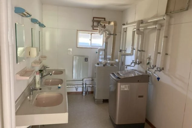 三つの洗面台がある共用洗面所。部屋には洗濯機があり、むき出しの配管が見える。