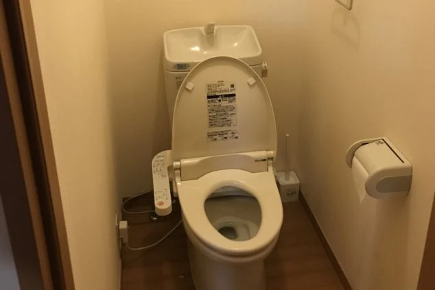 寮のトイレ。手洗い付きタンクと温水洗浄便座が設置された、清潔感のある洋式トイレ。