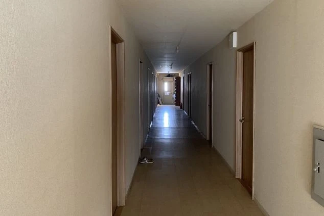 暖色の照明に照らされた、狭い廊下の写真。廊下の両側にはドアがいくつか見える。突き当たりには窓があり、光が差し込んでいる。