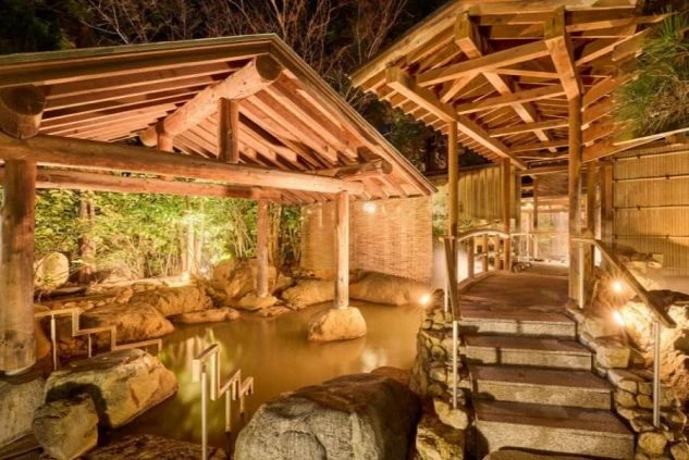 旅館やホテルの敷地内にある、岩と木々に囲まれた露天風呂の画像。リゾートバイトの仕事終わりに温泉で疲れを癒すイメージ。