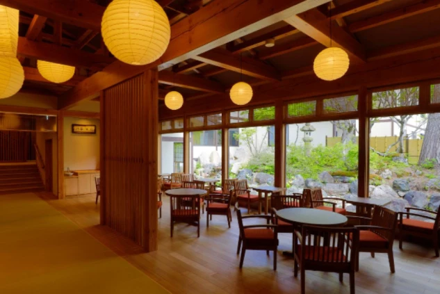 提灯の優しい光が灯る、日本庭園を望む和モダンな旅館ロビーの画像。