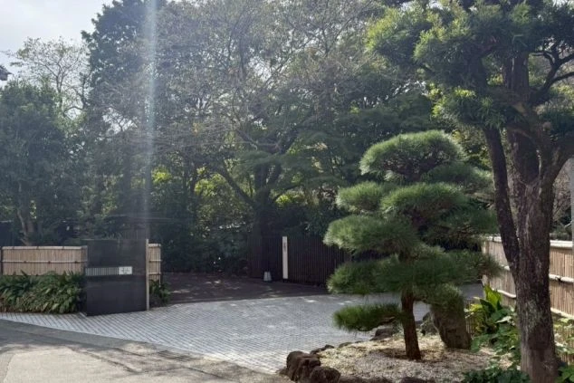 入口付近。手前に手入れされた松の木があり、竹垣と黒い門扉が見える。奥は鬱蒼とした木々で覆われ、リゾートのような雰囲気を醸し出している。
