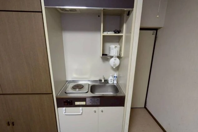 寮の各個室に備え付けられたミニキッチンの画像。電気コンロとシンク、炊飯器を置ける棚がある。