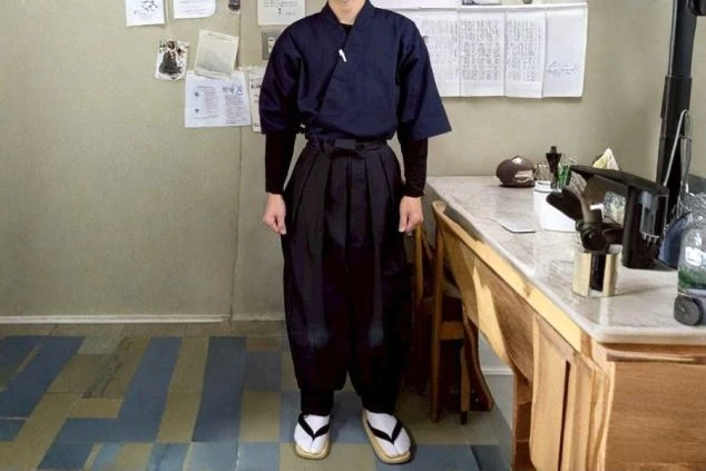 男性の仲居スタッフ用制服画像。濃紺の上着に袴を合わせた、伝統と動きやすさを兼ね備えた作務衣スタイル。