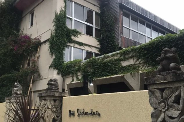 建物は蔦や緑の植物に覆われ、壁の下部には花やカエルをモチーフにした石像が置かれている。アジアンリゾートや隠れ家のような雰囲気がある。