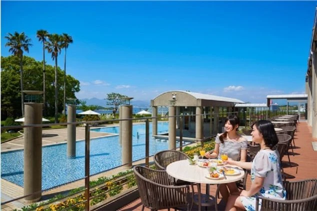 プールサイドのテラス席で、食事を楽しむ二人の女性。ヤシの木が立ち並ぶ、南国情緒あふれるリゾートホテルでの優雅なひとときです。