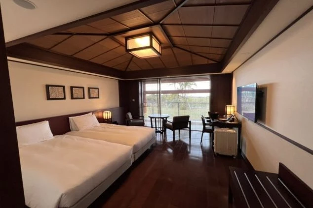 木製の格天井とフローリングが特徴的な、ツインベッドと窓際のテーブルセットがある洋室。