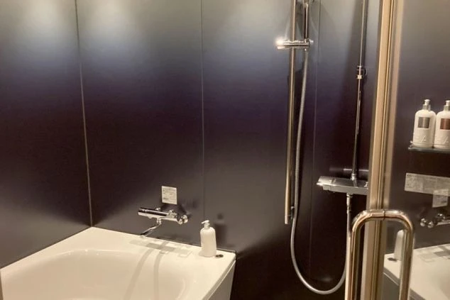 黒い壁に白い浴槽とシャワーが備え付けられた、モダンでシンプルなユニットバス