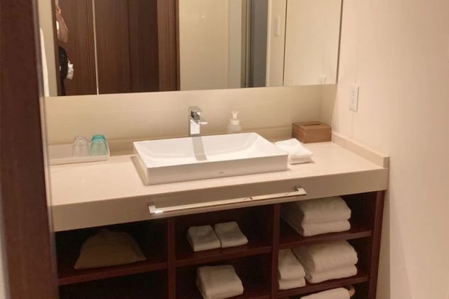 大きな鏡と白い洗面ボウル、下の棚にタオルが整理されたモダンな洗面台。