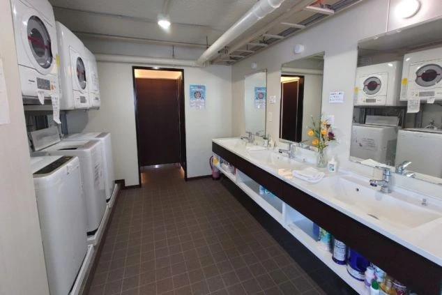 寮のランドリースペース。洗濯機と乾燥機が複数設置されており、仕事仲間と利用する様子。