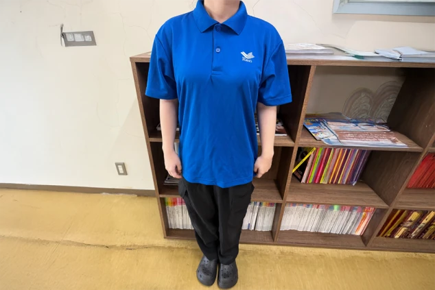  青いポロシャツと黒いズボン、サンダルを着用した人物の全身。