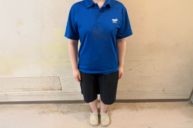 青いポロシャツと黒いハーフパンツ、サンダルを着用した人物の全身。