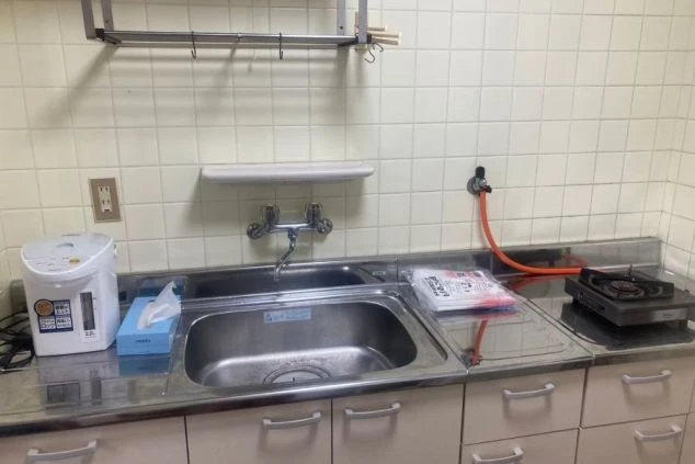 リゾートバイト寮の共用キッチン。ガスコンロ、シンク、電気ポットが備え付けらた便利な設備の画像。