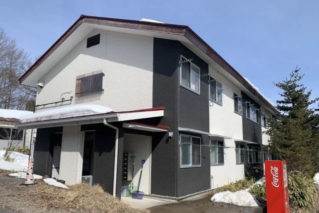 暖色の照明に照らされた、狭い廊下の写真。廊下の両側にはドアがいくつか見える。突き当たりには窓があり、光が差し込んでいる。