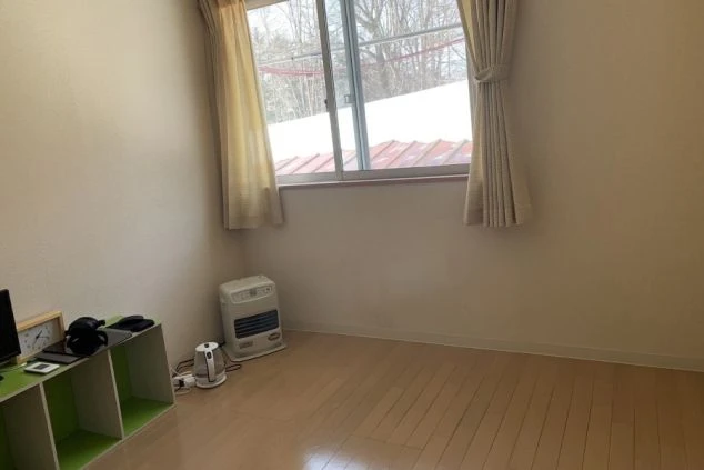 リゾートバイトの部屋の写真。奥には正方形の窓がありベージュのカーテンがかかっている。窓からは外の景色が見える。