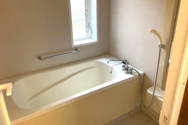 リゾートバイトの寮の浴室の画像。清潔感のある浴槽とシャワーが備え付けられており、窓から明るい光が差し込む。リラックスして入浴できる寮の設備。