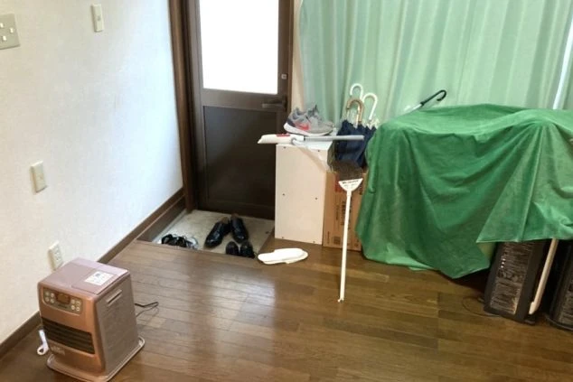 リゾートバイトの寮の玄関の画像。ドアのそばには靴が並び、暖房器具や傘立て、荷物が置かれている。生活感のある入り口の様子。