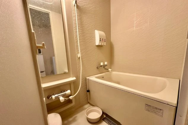 寮のユニットバス。浴槽、シャワー、シンク、鏡が一体となった清潔な空間が映る。