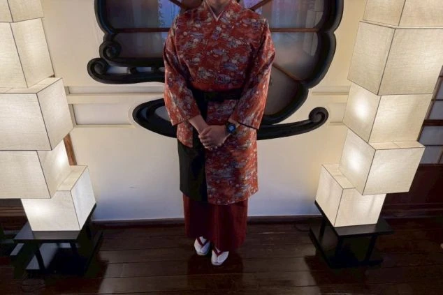 赤地に華やかな和柄の着物に、濃い色の袴と黒いエプロンを合わせたスタイル。足元は白足袋と草履。