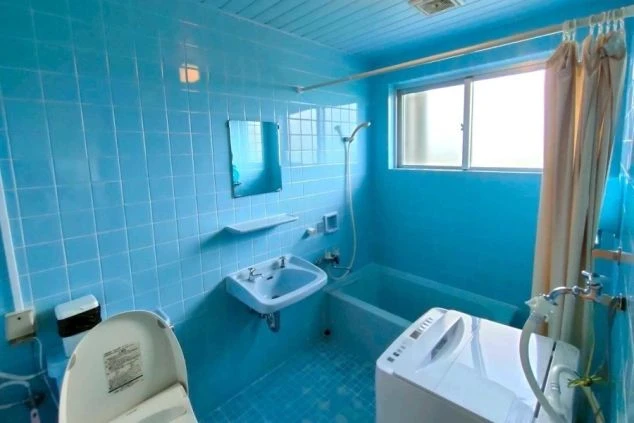 清潔感のある水色のタイルが特徴的な、バス・トイレ・洗面台完備の寮のユニットバスの画像。