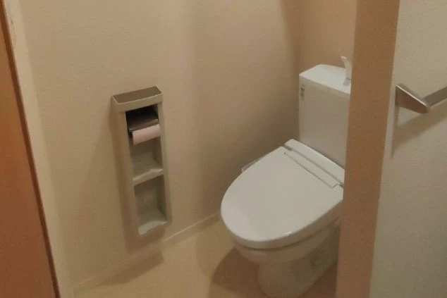 トイレットペーパーホルダー付きの棚と温水洗浄便座が設置されたトイレ。