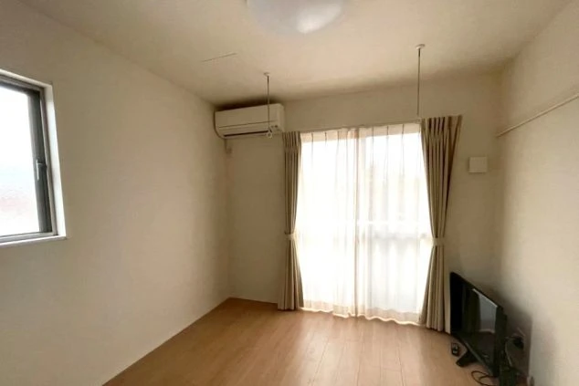 フローリングと白い壁の、エアコンとテレビがある明るい部屋。