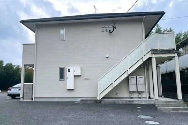 白い外壁の2階建て集合住宅の外観。外階段と駐車場。