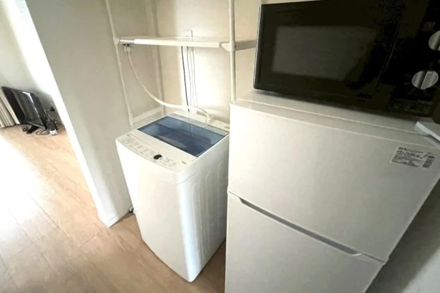 洗濯機と小型冷蔵庫、電子レンジが設置された収納スペース。