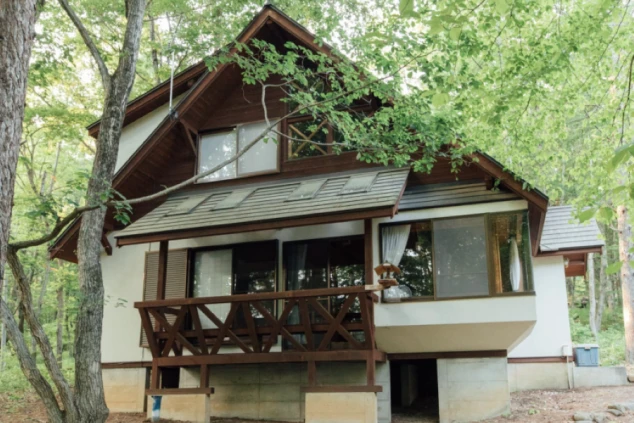 森林の中にある寮の外観の画像。三角屋根のロッジ風の建物で、バルコニーが特徴的。リゾートバイトの滞在施設としての外観イメージ。