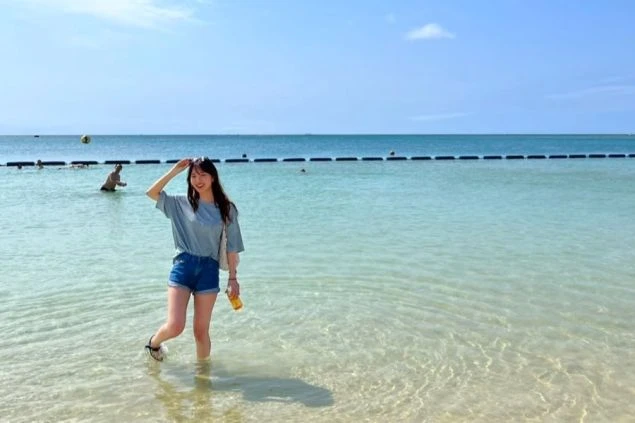 沖縄本島中部のアラハビーチで透明度の高い海に入って笑顔を見せる女性。リゾートバイトのオフにビーチでリフレッシュしたい方や、海が好きで沖縄での住み込みバイトを探している方に最適なワクトリオリジナル画像。